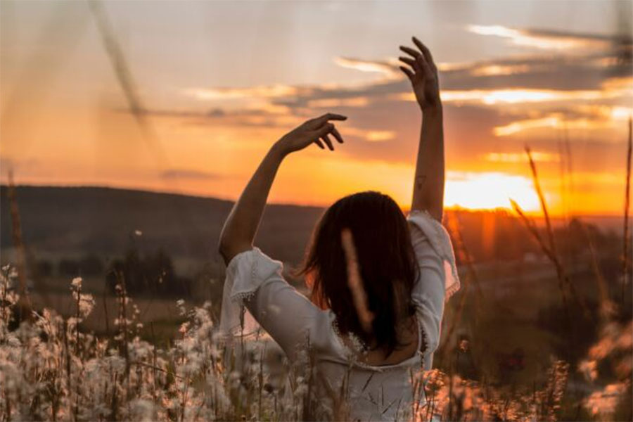 Woman hands in air in fields at sunset