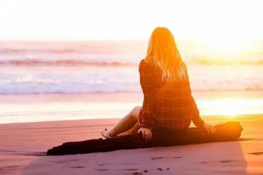 Woman sitting on log looking out to sea at sunset
